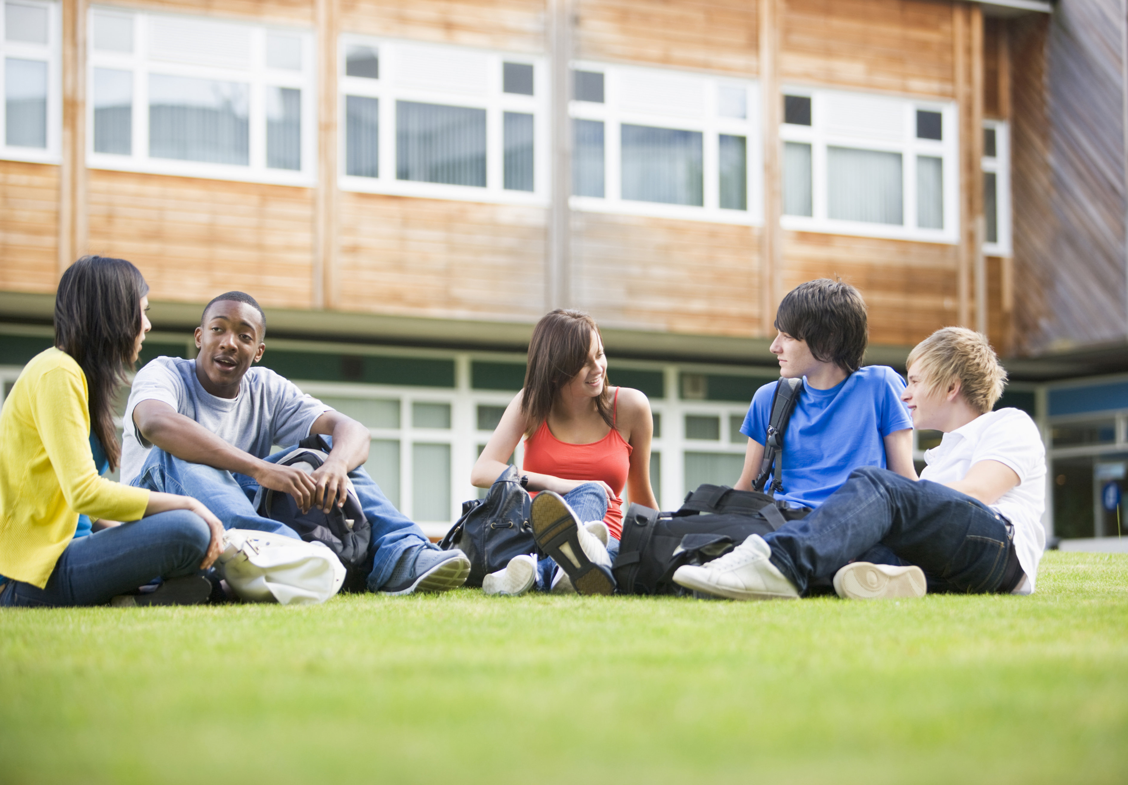 Five students sitting outdoors on lawn talking
