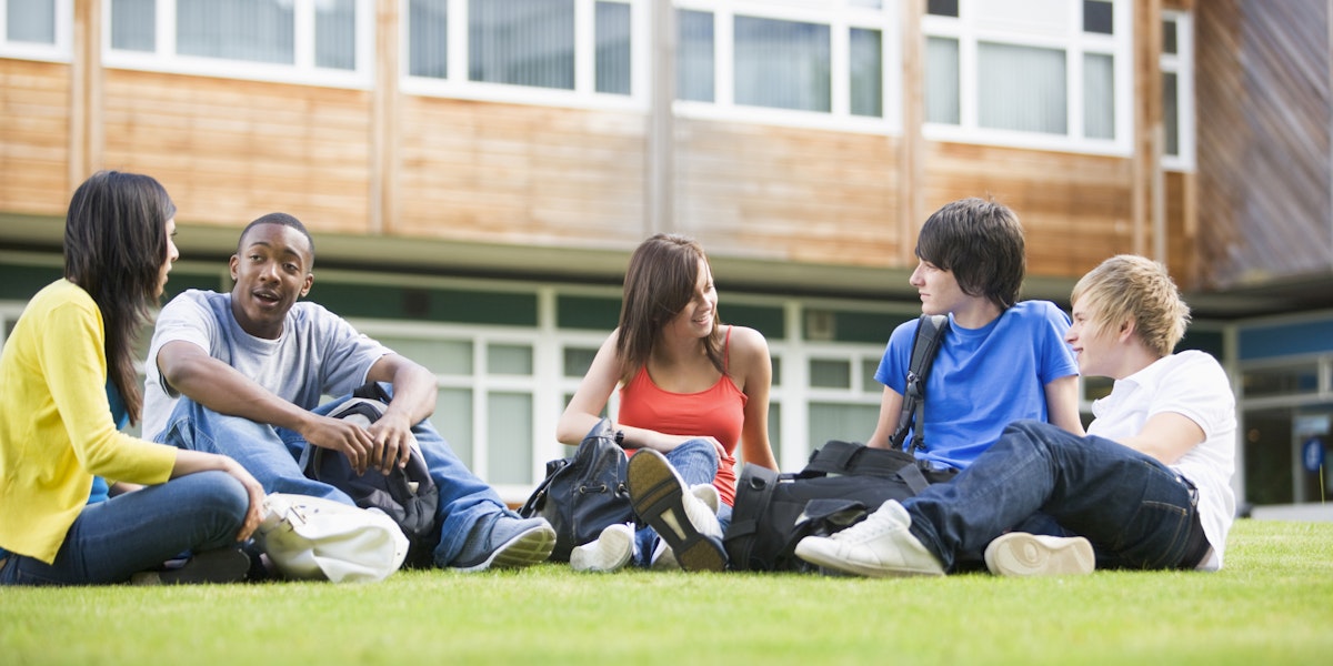 Five students sitting outdoors on lawn talking