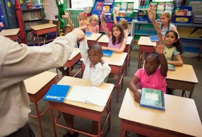 Multicultural kids raising their hands in a classroom