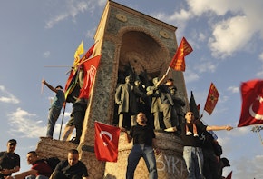 Men standing on a Turkish statue with flags