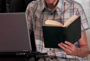 Student writing a paper from a book on a notebook computer