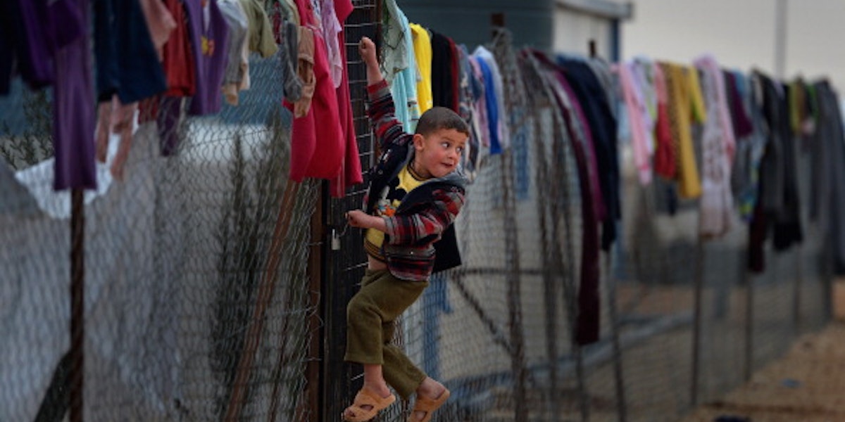 ZA'ATARI, JORDAN - FEBRUARY 01:  Young boy hangs on a fence with clothing hung from it, as Syrian refugees go about their daily business in the Za'atari refugee camp on February 1, 2013 in Za'atari, Jordan. Record numbers of refugees are fleeing the violence and bombings in Syria to cross the borders to safety in northern Jordan and overwhelming the Za'atari camp. The Jordanian government are appealing for help with the influx of refugees as they struggle to cope with the sheer numbers arriving in the country.  (Photo by Jeff J Mitchell/Getty Images)