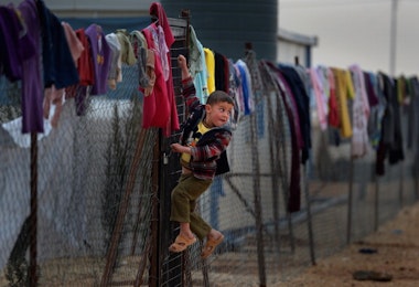 ZA'ATARI, JORDAN - FEBRUARY 01:  Young boy hangs on a fence with clothing hung from it, as Syrian refugees go about their daily business in the Za'atari refugee camp on February 1, 2013 in Za'atari, Jordan. Record numbers of refugees are fleeing the violence and bombings in Syria to cross the borders to safety in northern Jordan and overwhelming the Za'atari camp. The Jordanian government are appealing for help with the influx of refugees as they struggle to cope with the sheer numbers arriving in the country.  (Photo by Jeff J Mitchell/Getty Images)