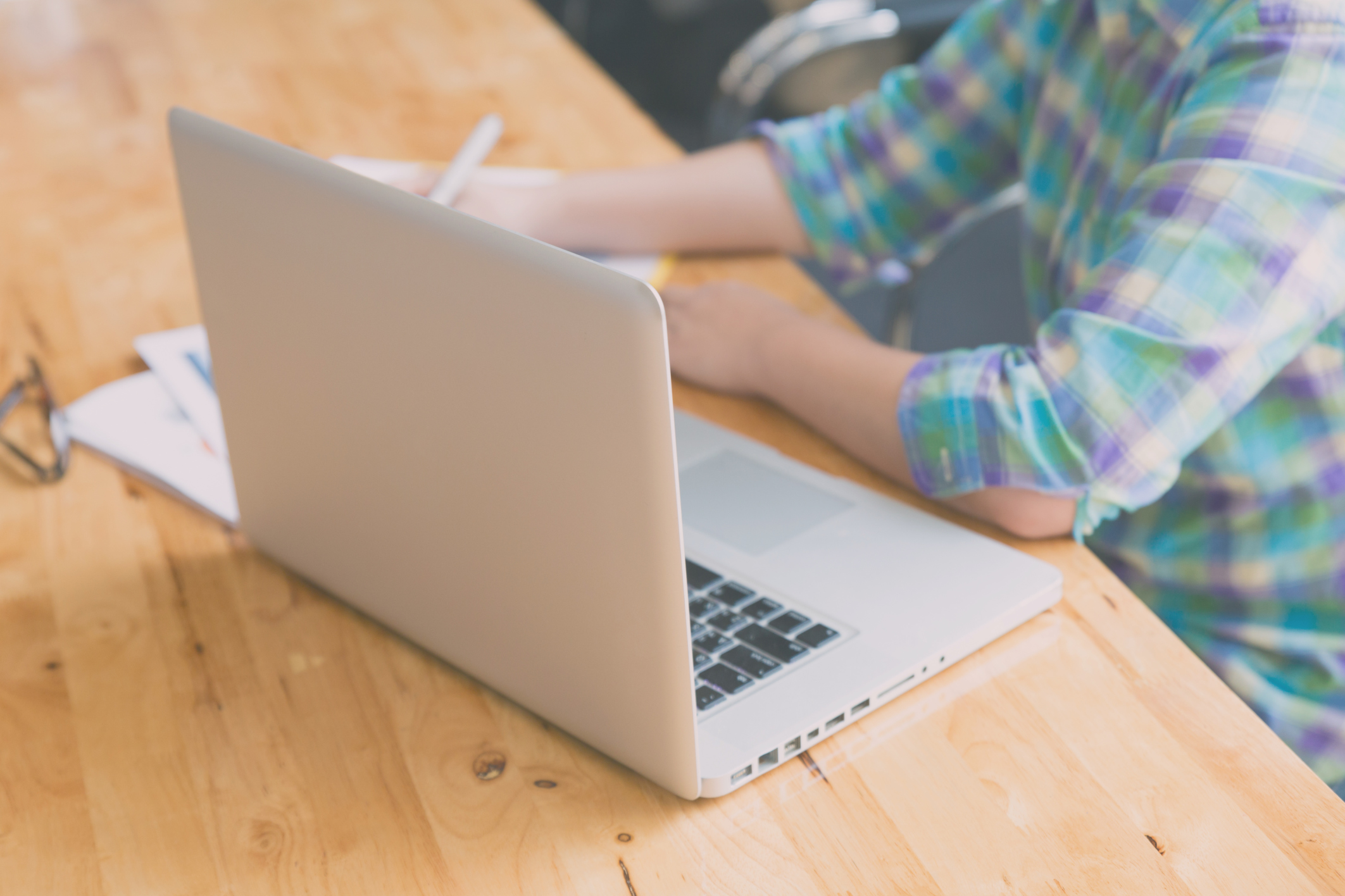 woman hand, pen, glasses, business document, laptop computer notebook on wooden table (vintage tone and color filter)