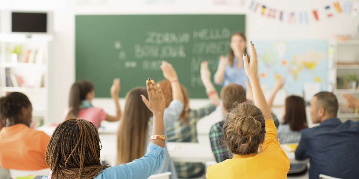 Two women in a multicultural classroom raising their hands