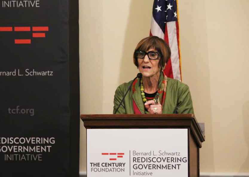 a woman standing at a podium in front of a flag