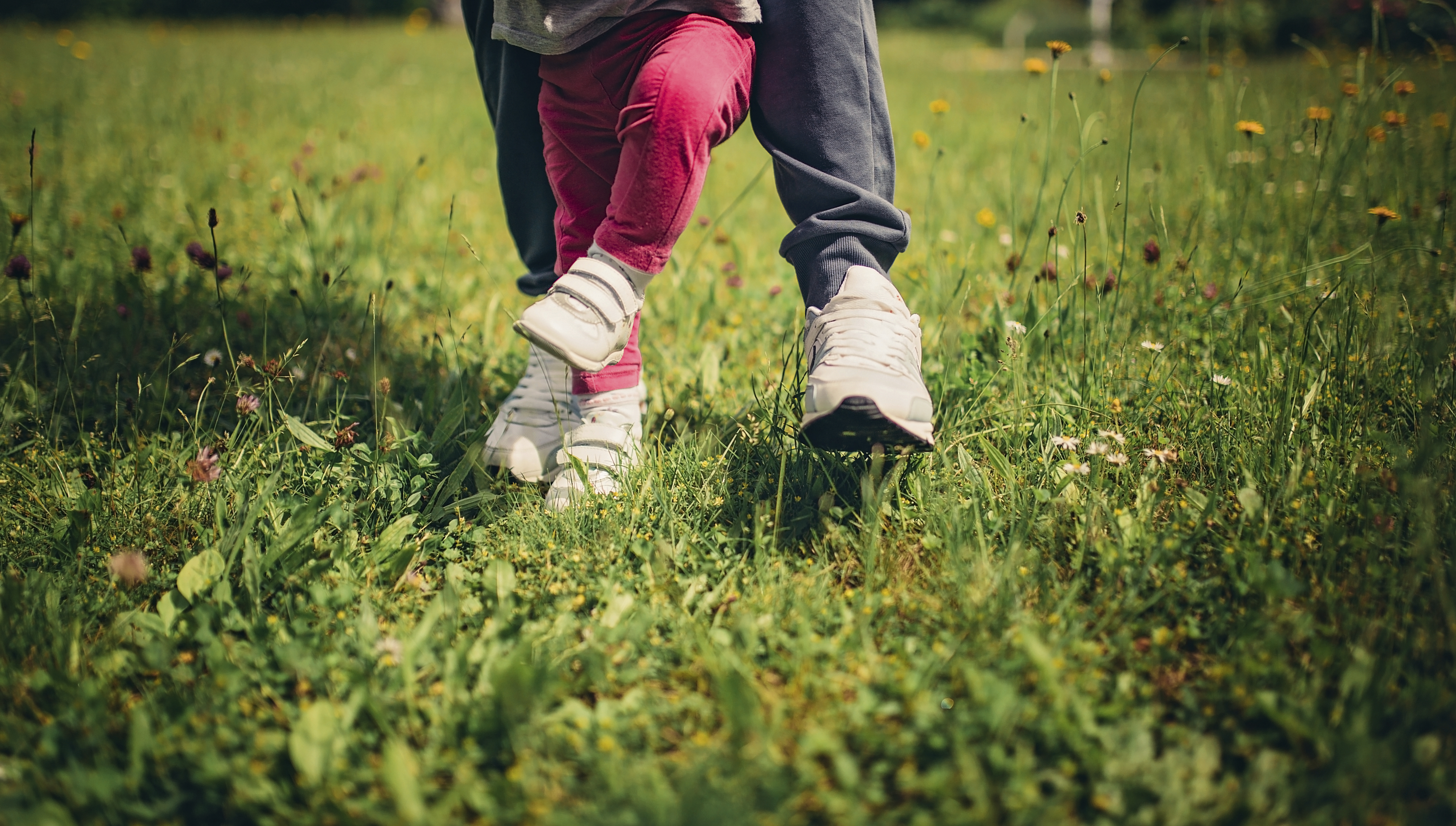 Mother helping her child to stand and walk on the grass