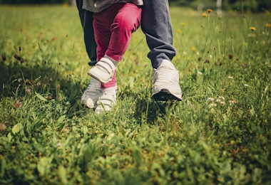 Mother helping her child to stand and walk on the grass