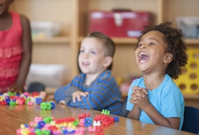 A multi-ethnic group of elementary age children are playing with toy blocks together at a table.
