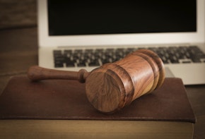 Wooden judge gavel on law book with laptop computer in background. Concept of cyber law or law about internet.
