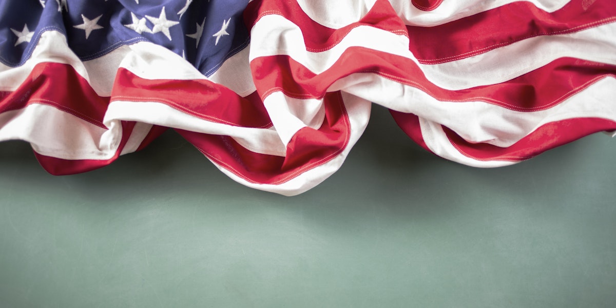 Red, white and blue American flag in front of a school classroom green chalkboard. USA education with copyspace at bottom. No people.