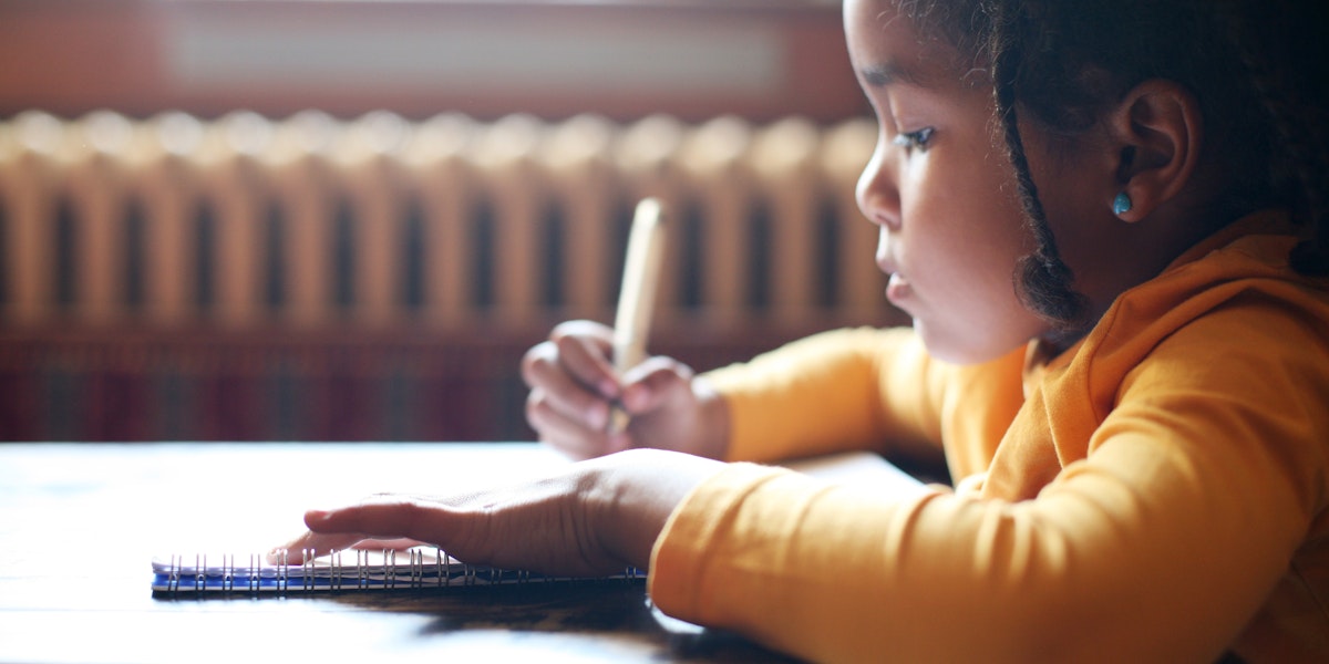Profile of little African girl writing in classroom.