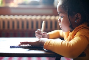 Profile of little African girl writing  in classroom.