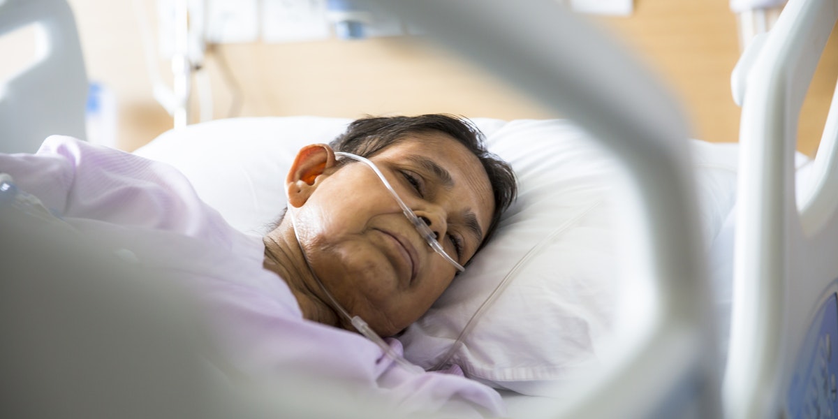 Old woman patient lying on Hospital bed with Oxygen tubes in her nose. She has her eyes closed.