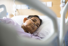 Old woman patient lying on Hospital bed with Oxygen tubes in her nose. She has her eyes closed.