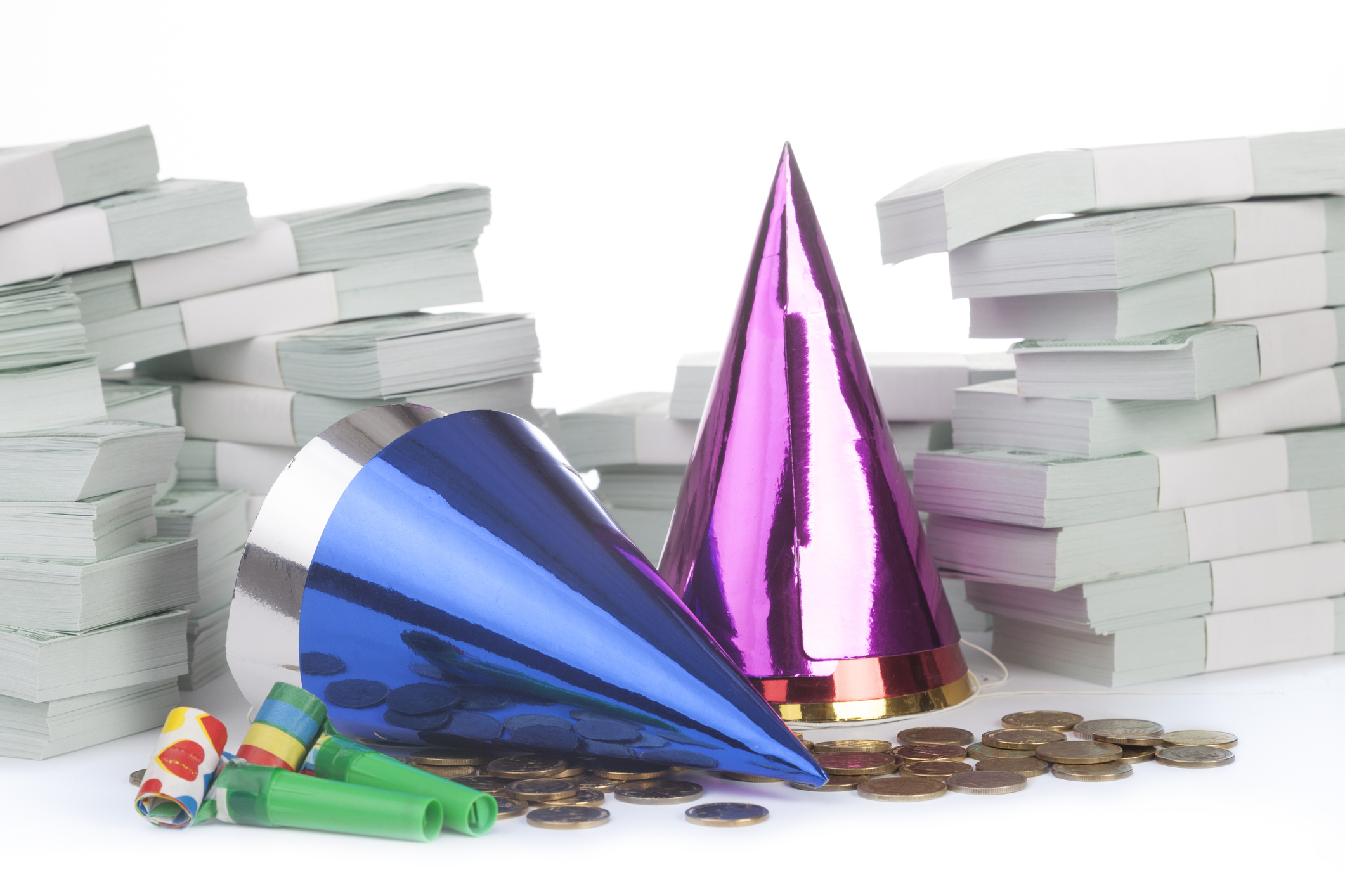 Stack of money with party horn blower and little hats isolated on white