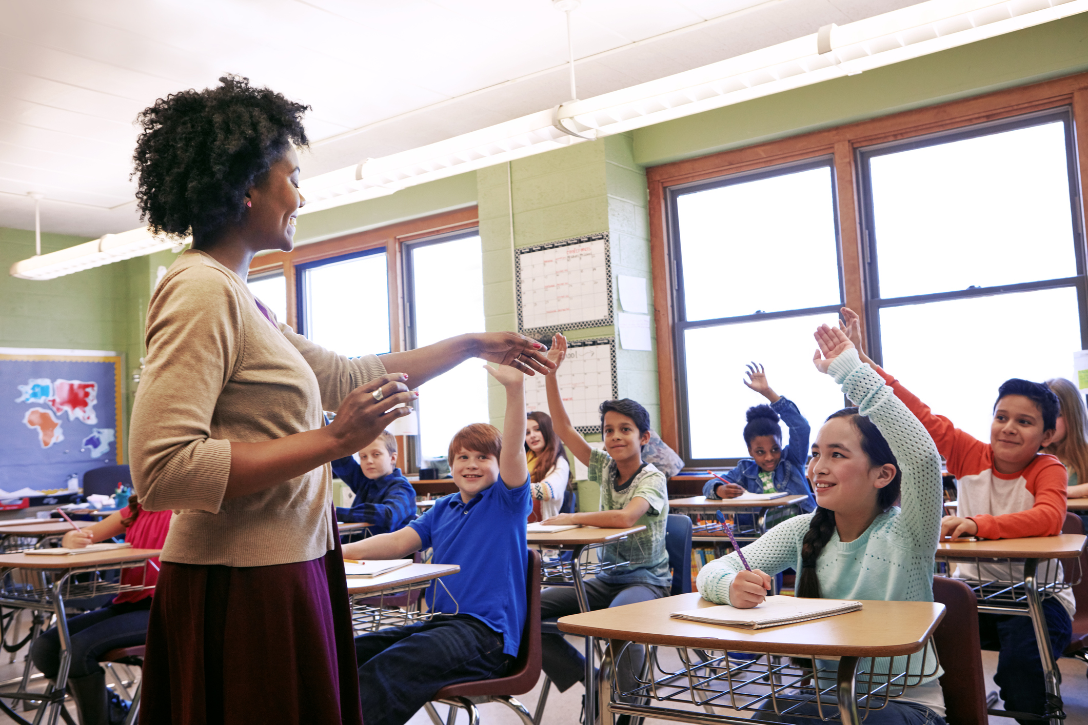 Shot of a group of children raising their hands to answer their teacher's question