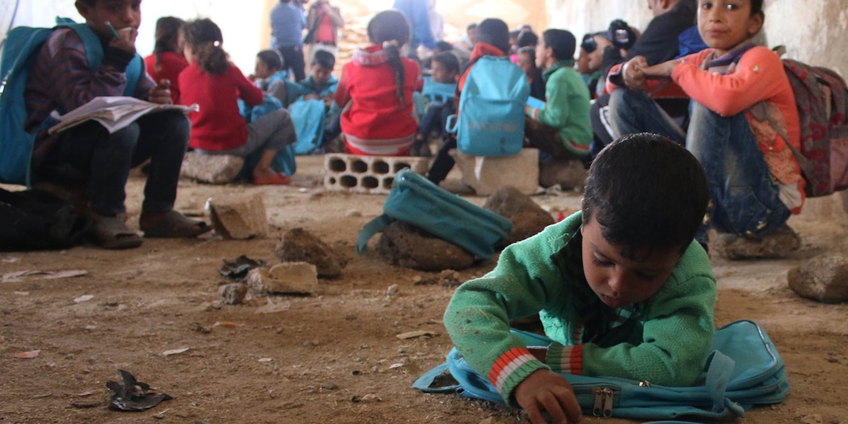 On 13 November 2016, children lie or sit on the ground writing in notebooks at a make-shift school in rural Dar'a in the Syrian Arab Republic. Despite the ongoing violence across the country, children and dedicated teachers are doing all they can to keep their education going. Some 1.7 million children are currently (Nov 2016) out of school in the Syrian Arab Republic. Schools across the Syrian Arab Republic continue to be destroyed and damaged. This year (2016) 84 attacks on schools have resulted in the deaths of 69 children. UNICEF has provided 3.2 million children with learning materials, such as school bags, stationary and text books.

In November 2016, there is no safe place for children to learn or play in Syria. Underground facilities including basements and even caves, are used to shelter children from a war they grew up knowing nothing else. Displaced families from different areas in rural Damascus and Dar’a sought refuge in tents in rural Dar’a. The make-shift school receives up to 80 children on a daily basis. They are grouped according to age and knowledge in four groups, where each of the four former teachers, displaced themselves, teaches them reading and writing in both Arabic and English and the principals of mathematics. “There is not a single space or even an extra tent that we could’ve used as a learning space,” says [NAME CHANGED] Muhammad, a teacher in this school. “So we had to clean this fodder collection centre and turn it to a school where almost 80 children come on a daily basis to learn reading and writing, both in Arabic and English, and the principals of mathematics,” Muhammad continues.  The children are divided into four groups based on their knowledge and age. Each group is taught by one of the four former teachers, two male and two female teachers. “Children have to share notebooks because we severely lack the necessary education supplies. They rotate on using the only six desks available.”  [NAME CHANGED] Mona, a