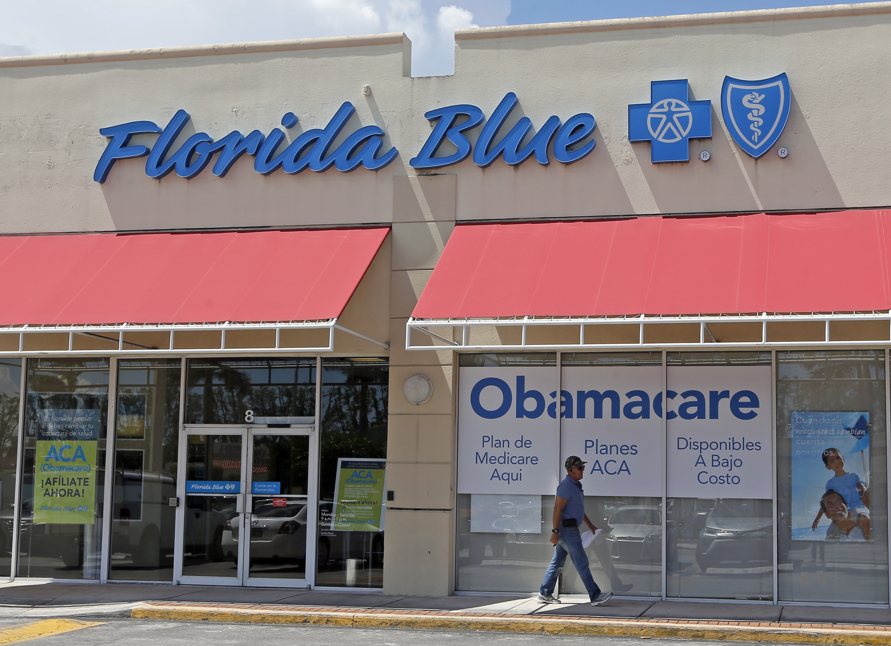 FILE - In this Thursday, July 27, 2017, file photo, a person walks by a health care insurance office in Hialeah, Fla. Health insurance shoppers will face a new deadline, rising prices and fewer options for help in many markets when the Affordable Care Act’s main enrollment window for 2018 coverage opens Wednesday, Nov. 1. Insurance experts say those who need insurance should avoid waiting to do last-minute shopping. (AP Photo/Alan Diaz, File)