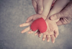 old hands holding young hands of a baby with red heart / Love and relationship in a family