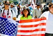 Los Angeles, USA - May 1, 2013: May Day March in Los Angeles Downtown, USA. People holding banners representing different social structures, organizations. March was mostly dedicated to Immigration reform discussed. Two women and teenager girl are holding big American flag.