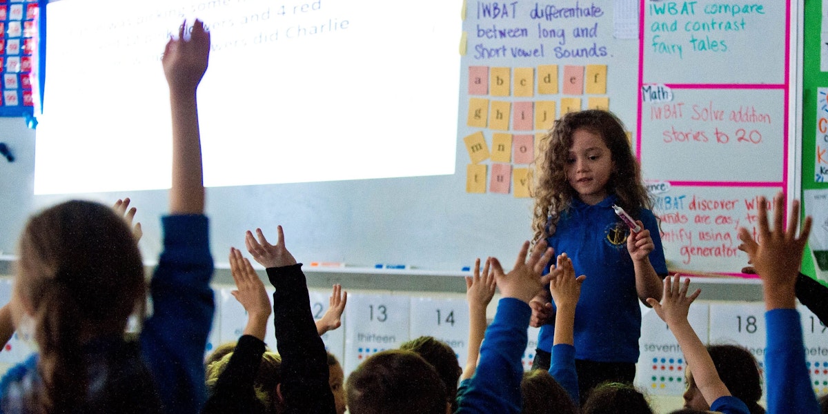 a group of children raising their hands in a classroom