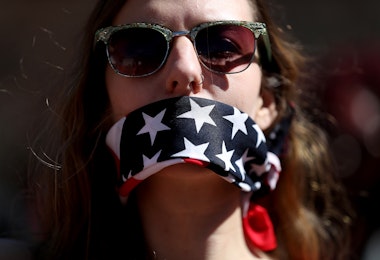 WASHINGTON, DC - MARCH 08: A protester wears a patriotic bandana over her mouth during a march and rally to support women's health programs and protest the White House global gag rule on March 8, 2017 in Washington, DC. Hundreds of women marked International Women's Day with a march and rally outside of the White House to protest the White House global gag rule and support women's health programs. (Photo by Justin Sullivan/Getty Images)