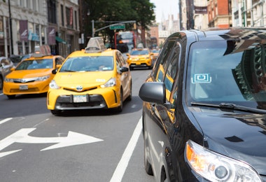 New York, USA - July 8, 2017: Uber car service in foreground picking up passenger on Broadway in Lower Manhattan shopping district. Customer call on an Uber car by using an app on the mobile phone