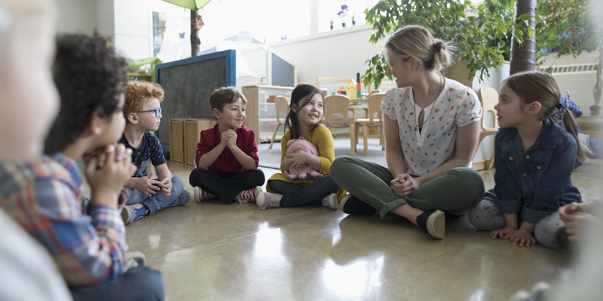 a group of children sitting on the floor talking to a woman