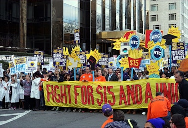 A photograph of a demonstration in a city advocating for the fight to raise the minimum wage.