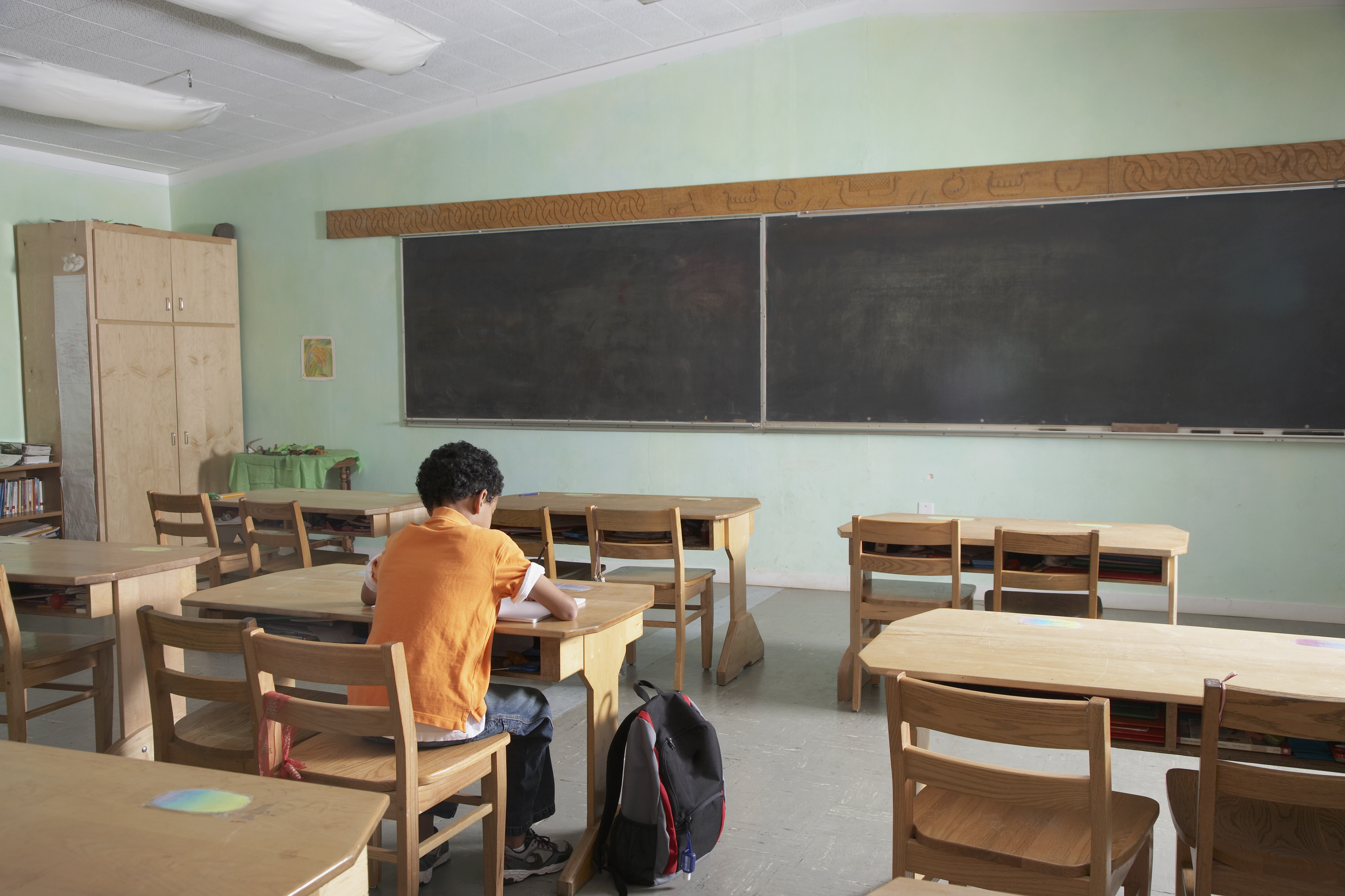 a boy sitting at a desk in front of a blackboard