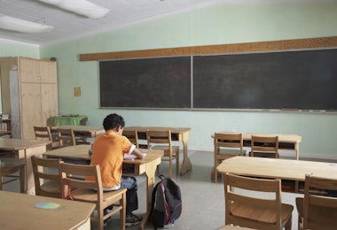 a boy sitting at a desk in front of a blackboard