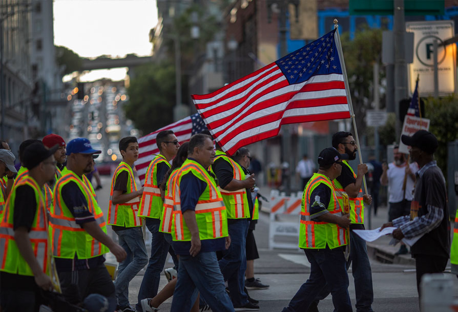 People walking with high visibility uniforms holding an american flag