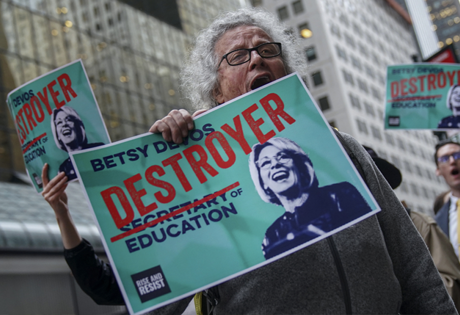 A demonstrator holding a poster saying Betsy the Destroyer of Education