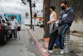 LOS ANGELES, CALIFORNIA  - APRIL 06: Young men wear face masks while waiting to clean windshields for extra cash amid the coronavirus pandemic on April 6, 2020 in south Los Angeles, California. More than 10,000 people have now died in the U.S. from COVID-19. (Photo by Mario Tama/Getty Images)