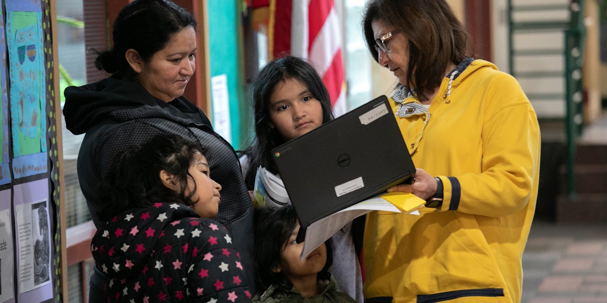 STAMFORD,  - MARCH 17: Bilingual teacher Maria Sanislo (R) explains a Google Chromebook to a family at KT Murphy Elementary School on March 17, 2020 in Stamford, Connecticut. Stamford Public Schools closed last week to help slow the spread of COVID-19, and students are now 