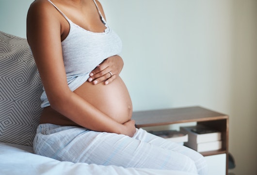 Shot of an unrecognizable pregnant woman sitting on a bed and holding her belly in her bedroom at home