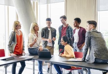 Casual students with female teacher in modern college building, woman in her 50s explaining to young people in their 20s