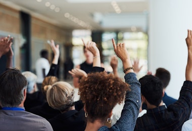 Shot of a group of businesspeople raising their hands to ask questions during a conference