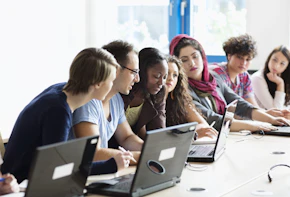 teacher explaining something to group of students in classroom with pc, sitting in a row,, focus on teacher