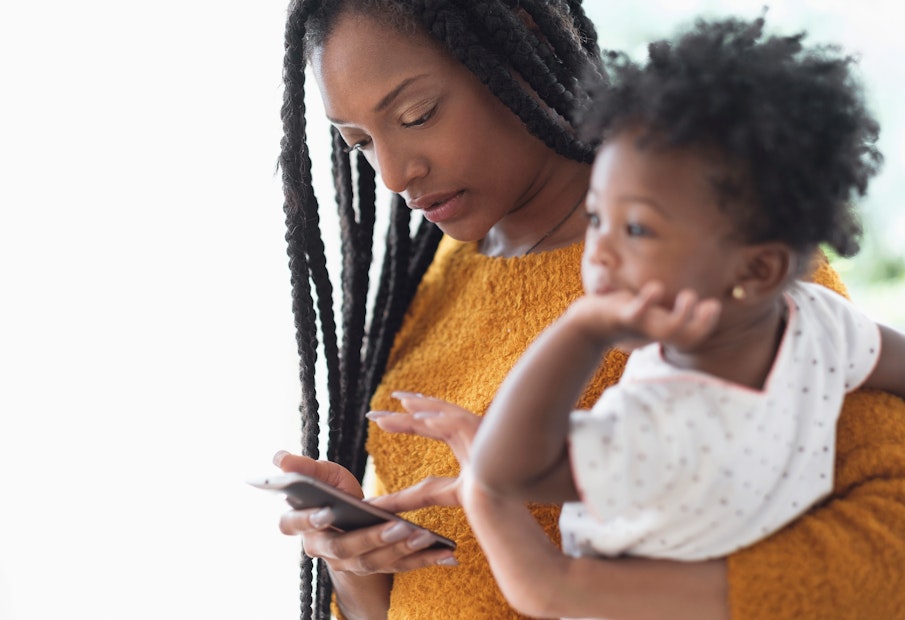 a woman holding a child while looking at a cell phone