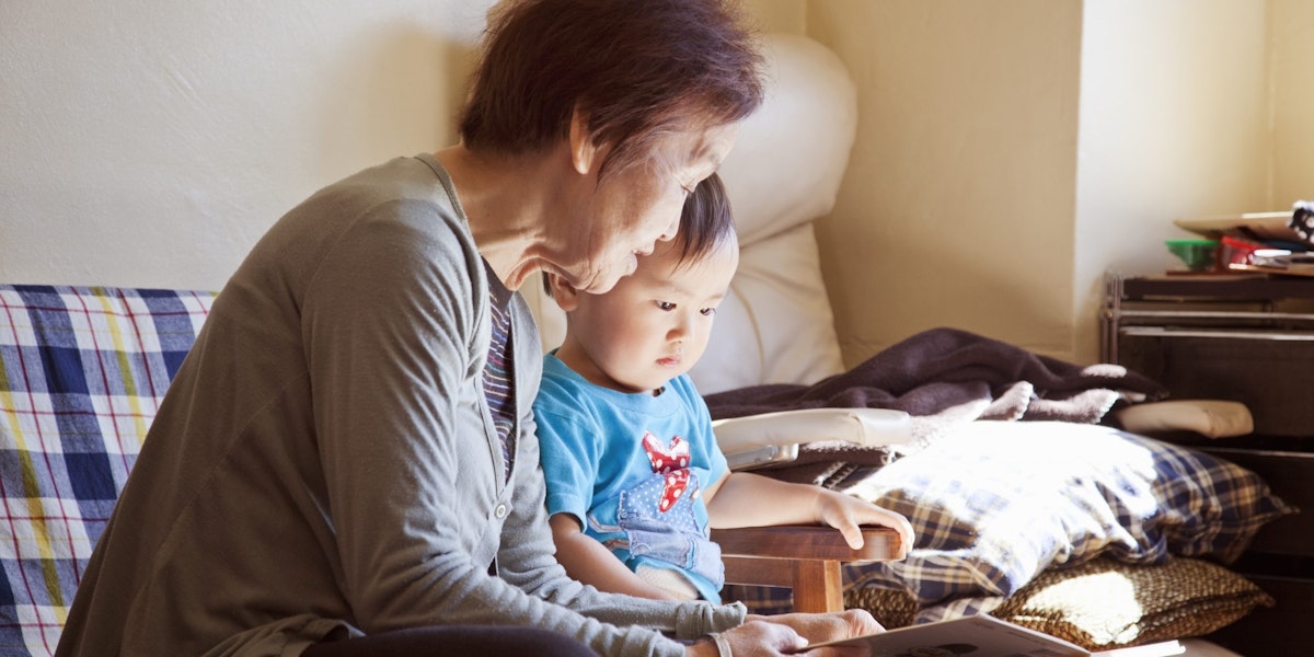 An asian grandmother reading out the picture book to her grandson at home.