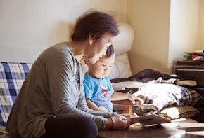 An asian grandmother reading out the picture book to her grandson at home.