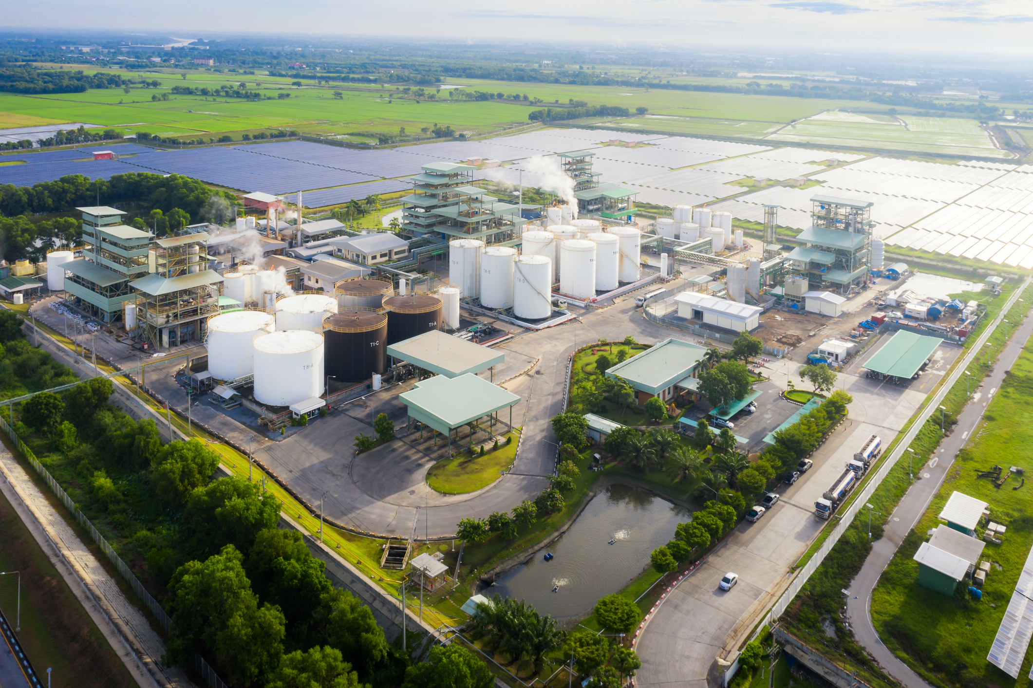 Aerial view photo of industrial zone showing oil refinery with storage tank with solar farm power station for renewable energy supply.
