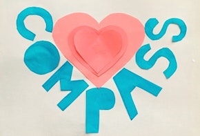 Children's artwork with a pink heart and the word Compass cut out of construction paper.