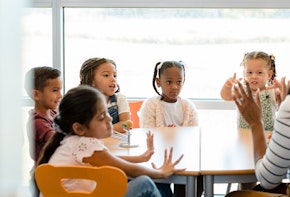 Sitting at a table in their classroom, a multi-ethnic group of preschool age children plays counting games with their unrecognizable female teacher.