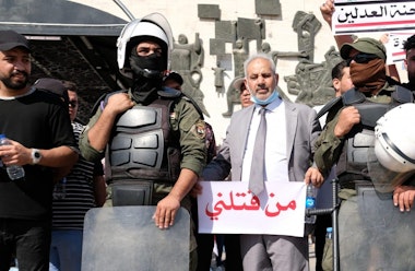 BAGHDAD, IRAQ - MAY 25: Protester stands next to police holding a sign saying 'who killed me' during anti-government protest on May 25, 2021 in Baghdad, Iraq. Protesters from across the country gathered in Baghdad demanding accountability after a recent rise in targeted assassinations. The protests used the slogan 'Who killed me' to highlight the recent killings of activists, journalists and human rights advocates. (Photo by Taha Hussein Ali/Getty Images)