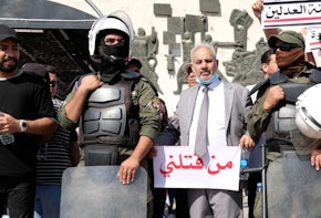 BAGHDAD, IRAQ - MAY 25: Protester stands next to police holding a sign saying 'who killed me' during anti-government protest on May 25, 2021 in Baghdad, Iraq. Protesters from across the country gathered in Baghdad demanding accountability after a recent rise in targeted assassinations. The protests used the slogan 'Who killed me' to highlight the recent killings of activists, journalists and human rights advocates. (Photo by Taha Hussein Ali/Getty Images)