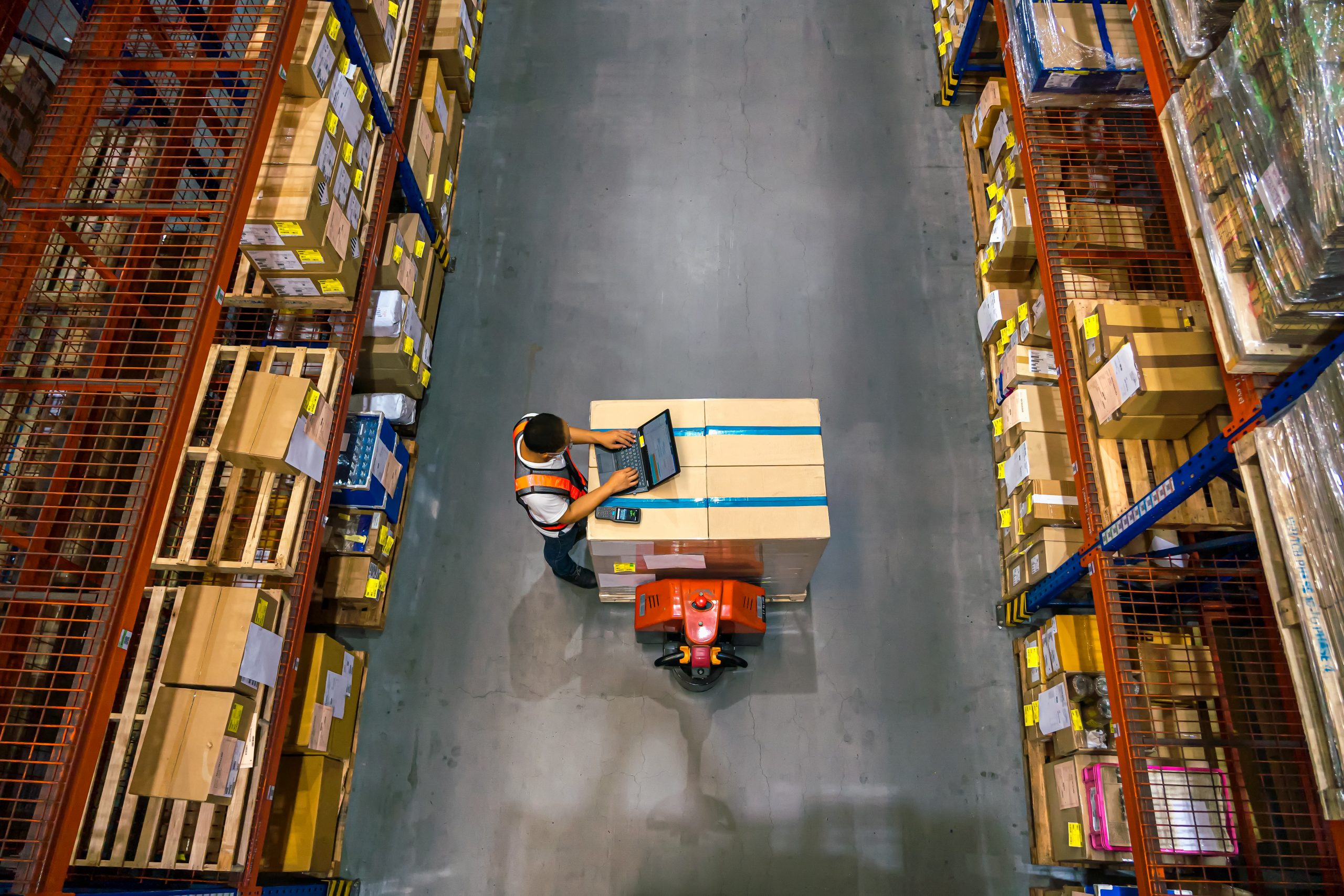 Top view of warehouse worker using laptop to check location of goods.