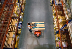 Top view of warehouse worker using laptop to check location of goods.